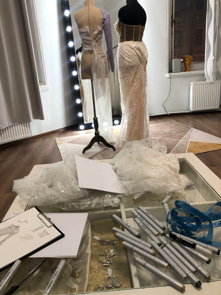 Atelier designer workspace with Copic markers, tape measure, and dress sketches — the setting of a real design conversation