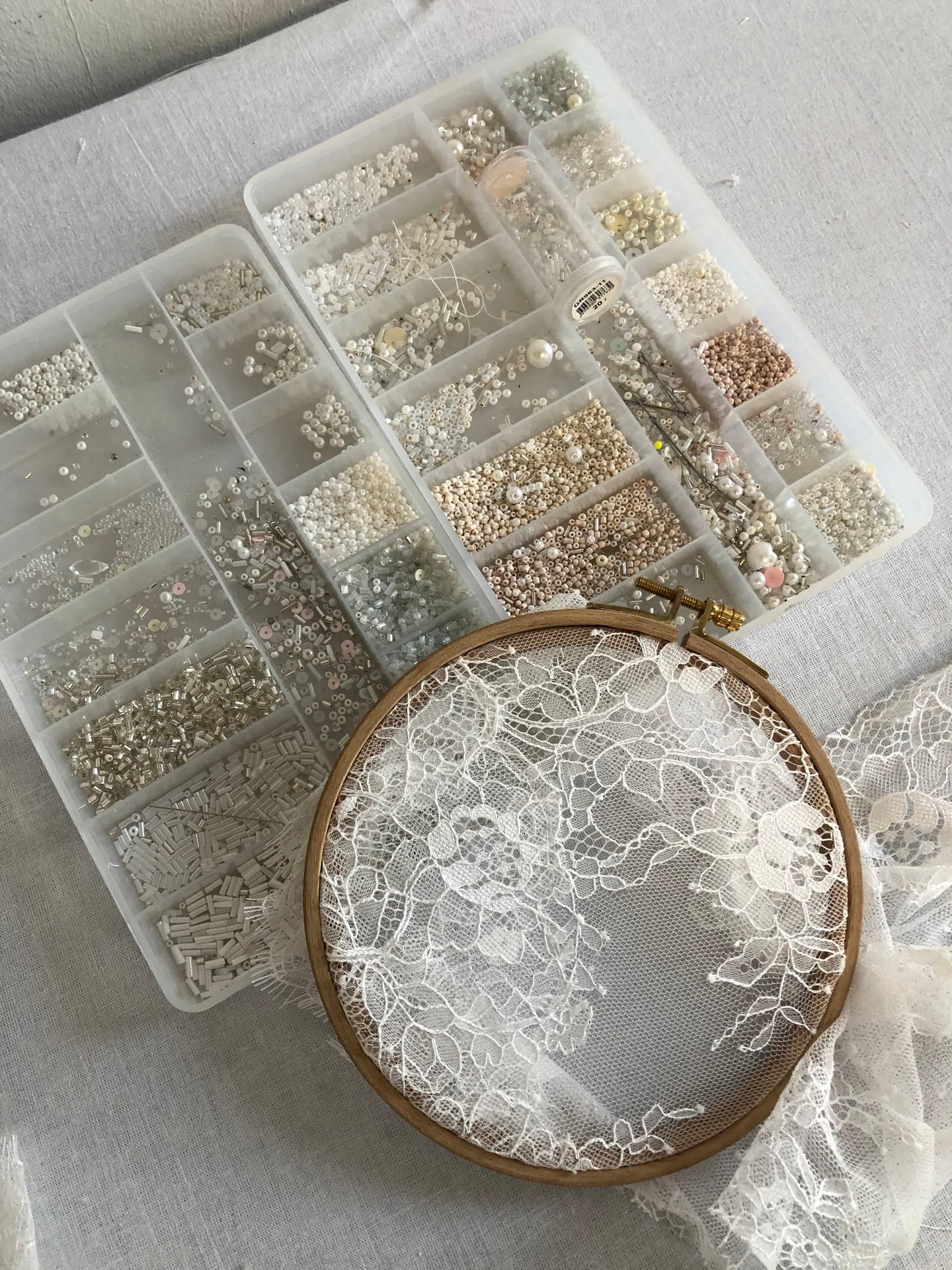 Overhead flat-lay of bridal beads, crystals, and pearls beside an embroidery hoop — materials for hand-applied wedding dress embellishment