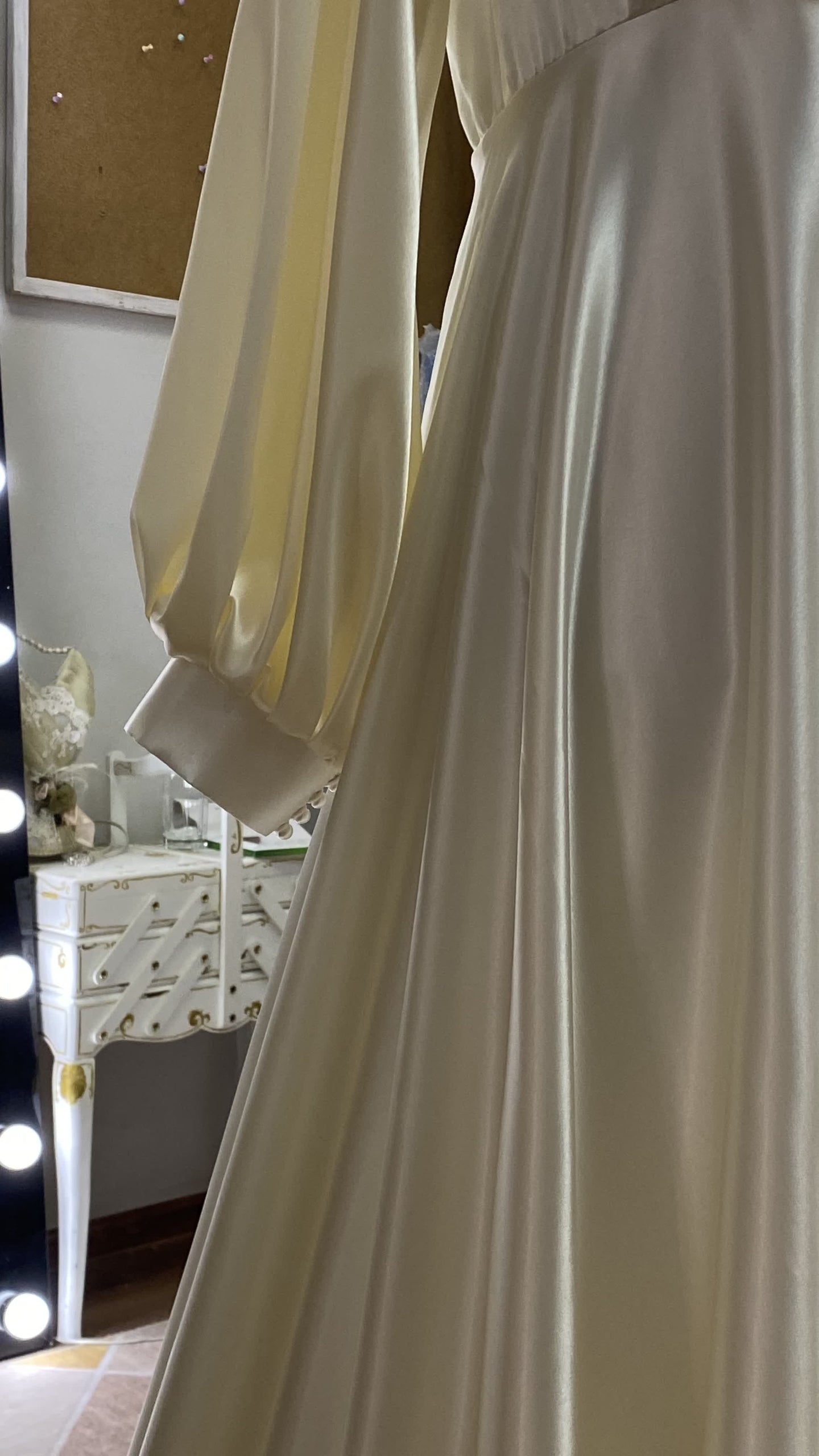 Detail of an ivory satin bishop sleeve cuff on a custom wedding dress, atelier furniture in the background