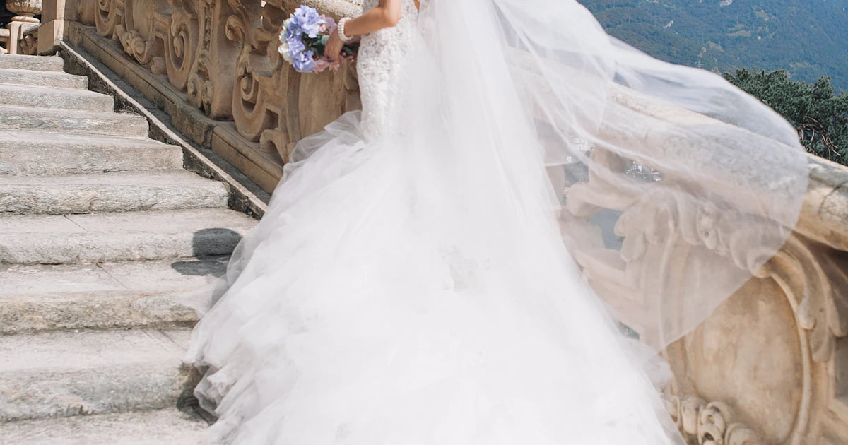 Bride in a flowing white wedding dress standing on white marble stairs holding a floral bouquet