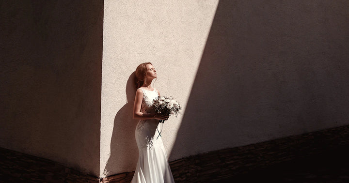 Bride in a sleek white satin mermaid gown with no embellishment standing against a dramatic light-and-shadow wall