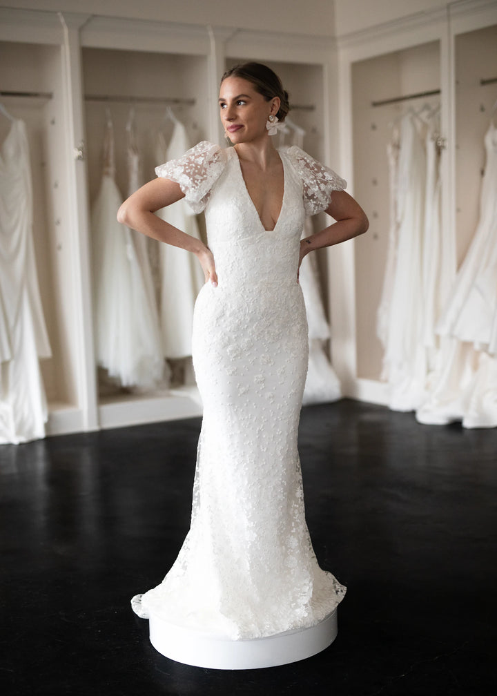 Bride standing in front of a row of wedding gowns in a bridal boutique