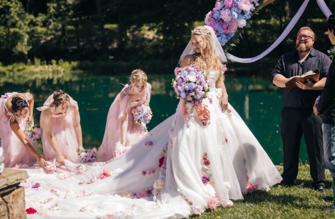 Cathedral train wedding dress at an outdoor lakeside ceremony — bridesmaids arranging the floral ballgown train on the grass